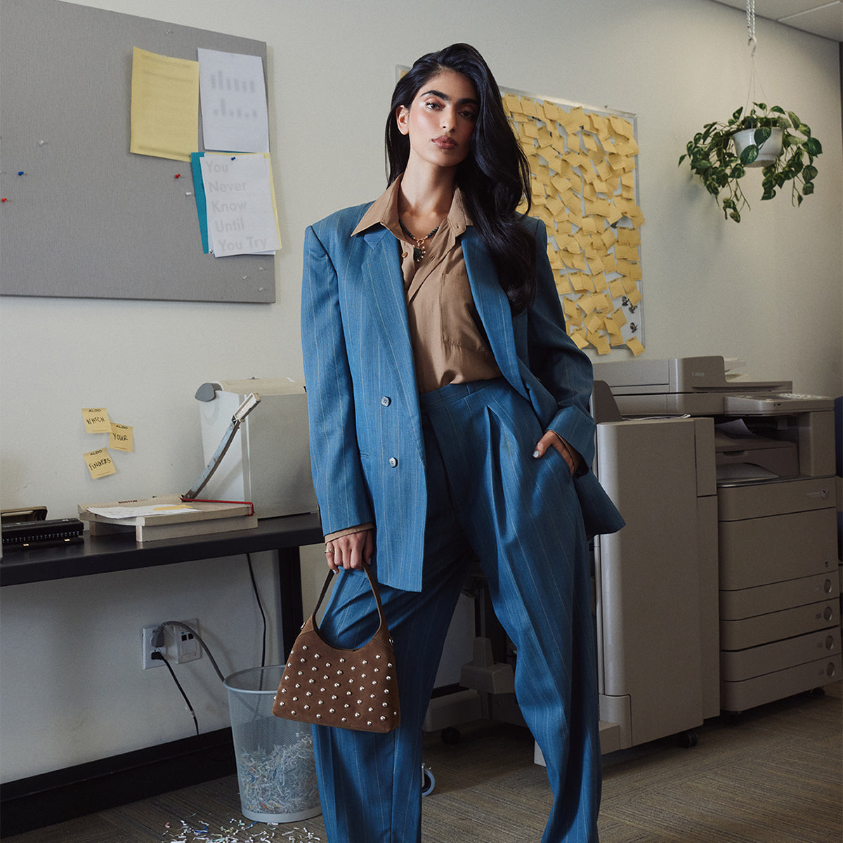 Woman in a blue suit standing in an office setting holding a brown bag