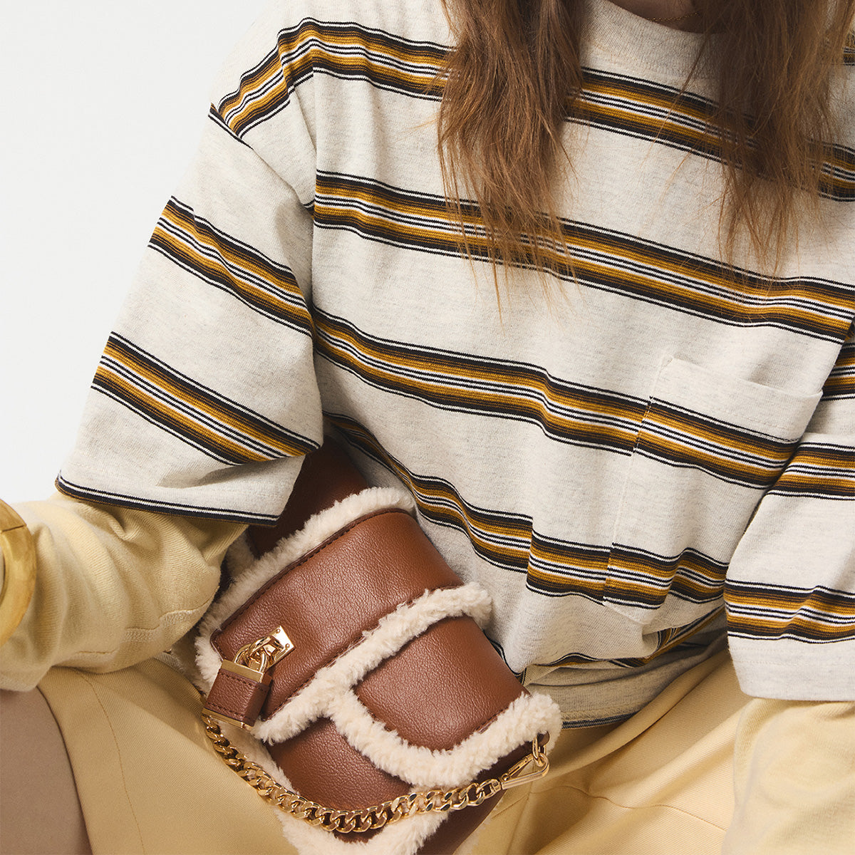 Person wearing a striped sweater holding a brown handbag with a gold chain.