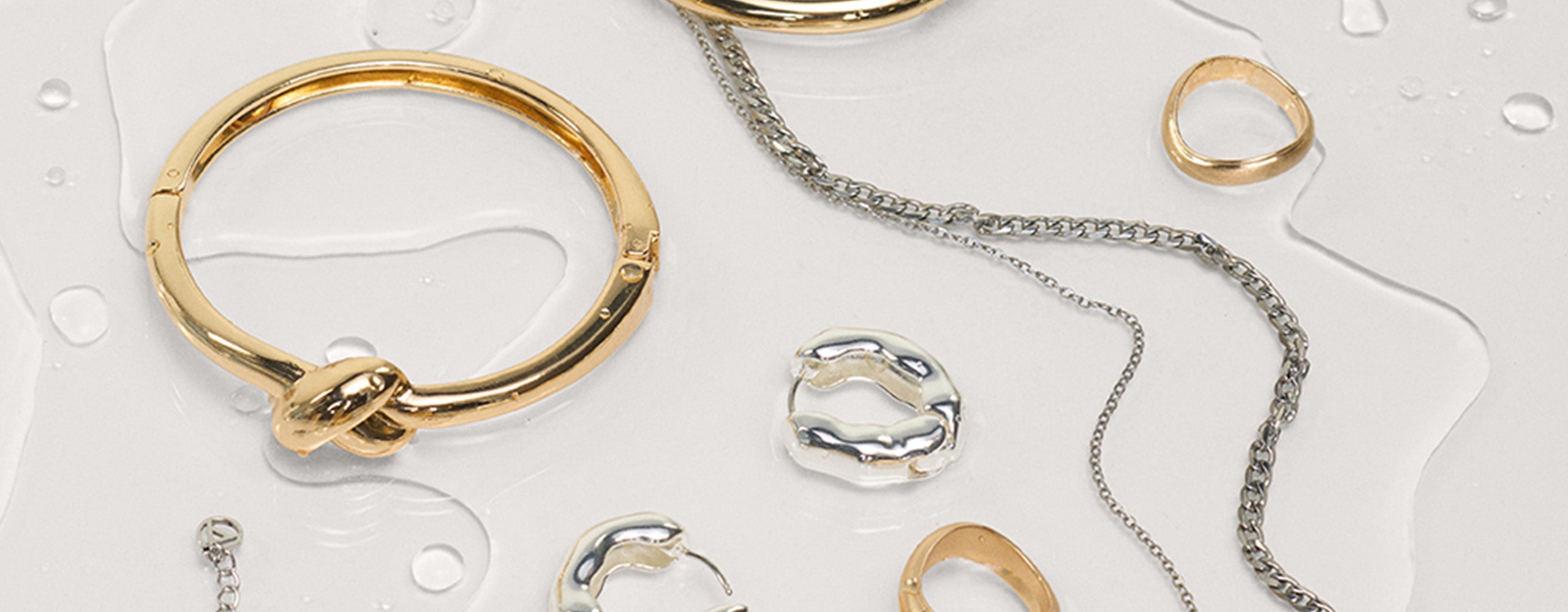 Collection of gold and silver jewelry including rings and a bracelet on a light background