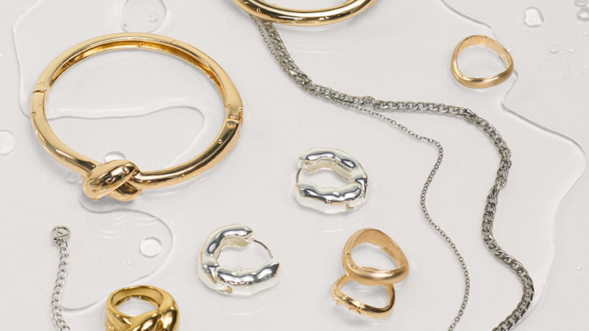 Collection of gold and silver jewelry including rings and a bracelet on a light background