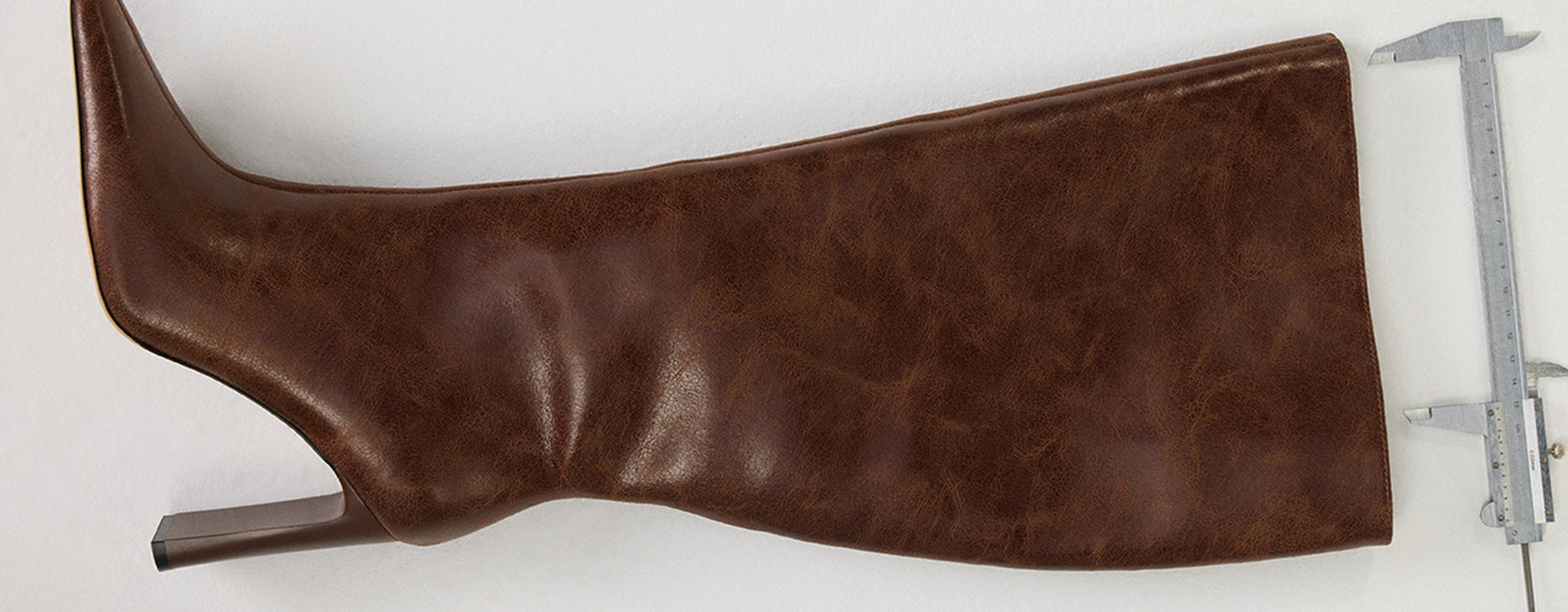 Brown leather boot on a white background with a caliper for scale.