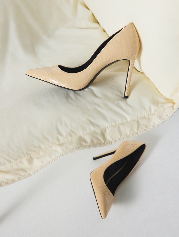 Une paire d’escarpins jaunes à bout pointu et à texture raffinée, présentée sur un tissu crème drapé.