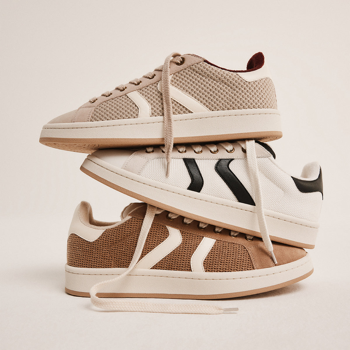 Three pairs of sneakers stacked on a light beige background