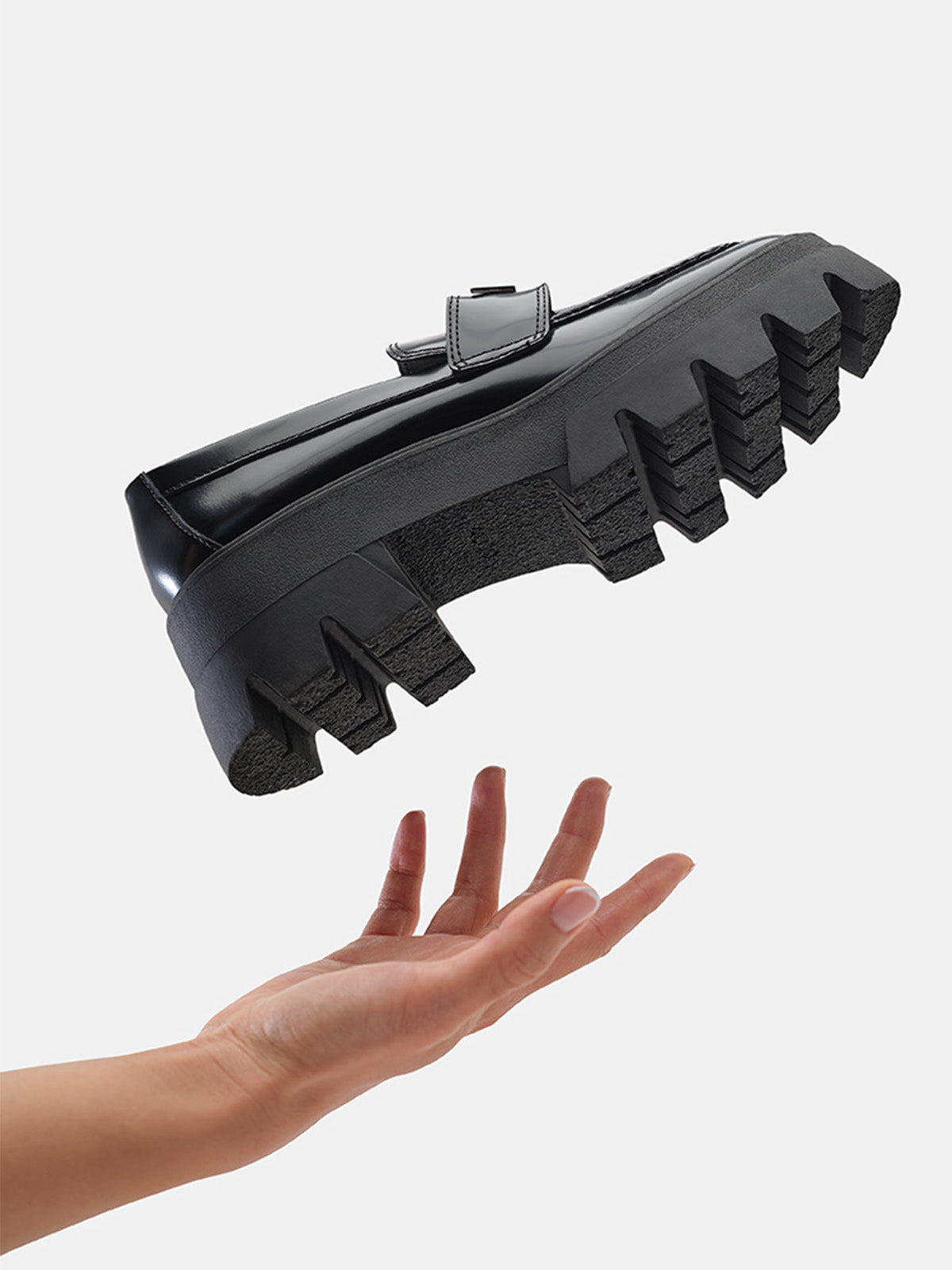 Black platform shoe hovering above a hand on a light gray background