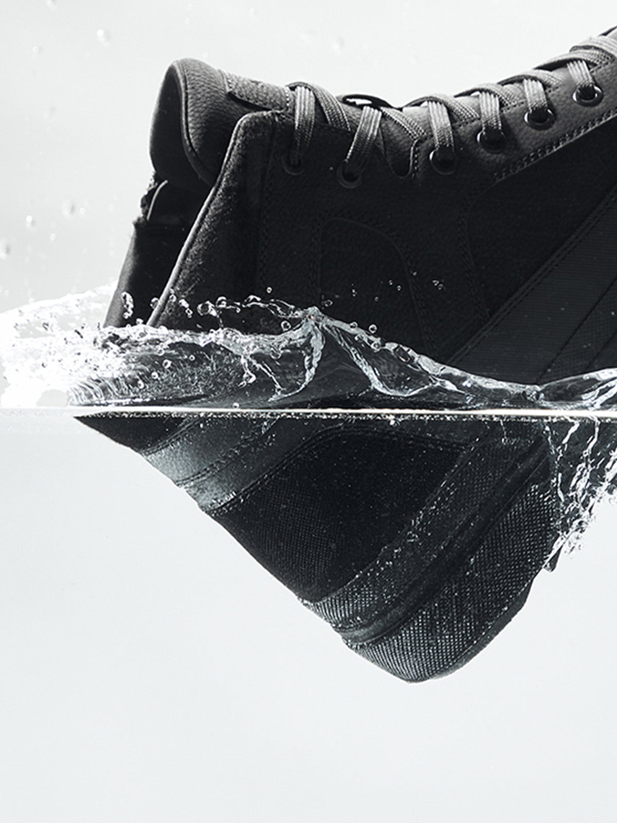 Black sneaker partially submerged in water with a white background