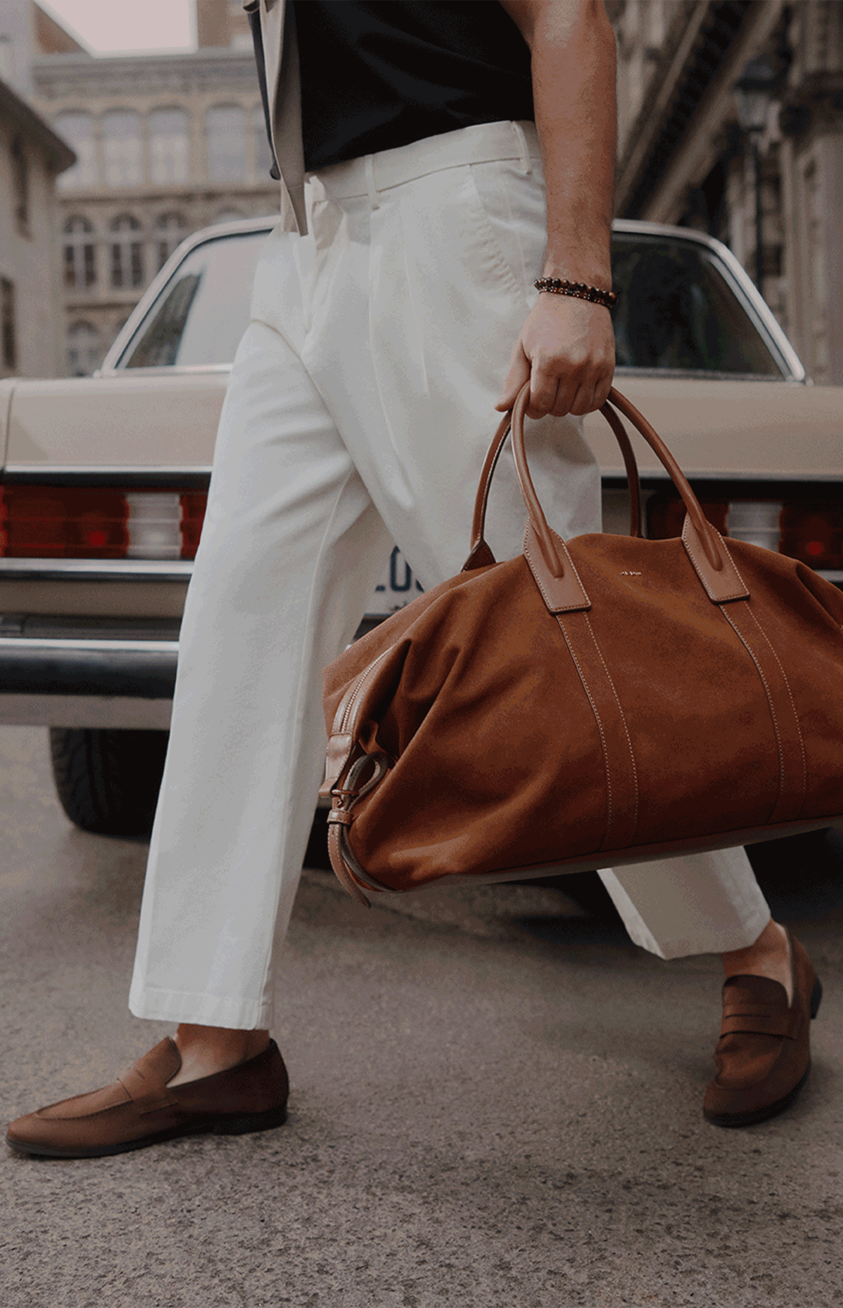 Une image de style de vie divisée montrant une femme portant une robe midi sans manches crème et tenant un sac à main blanc, ainsi qu’un homme en pantalon blanc transportant un sac de voyage en suède brun dans une rue urbaine.