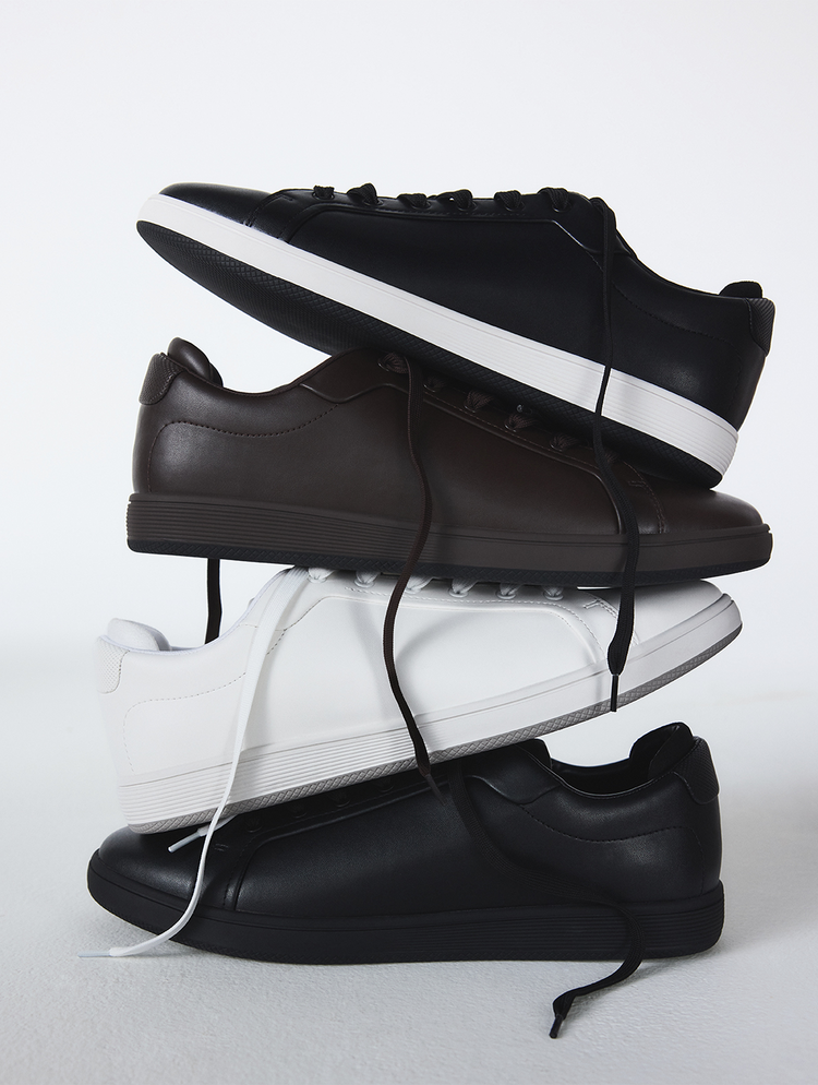 Une composition de quatre espadrilles minimalistes à tige basse empilées en forme de pyramide sur un fond de studio blanc. L’empilement comprend des espadrilles en cuir noires avec semelles blanches, des espadrilles en cuir brun foncé avec semelles blanches, des espadrilles en cuir blanches avec semelles noires, ainsi qu’une espadrille en cuir noire avec lacets blancs.