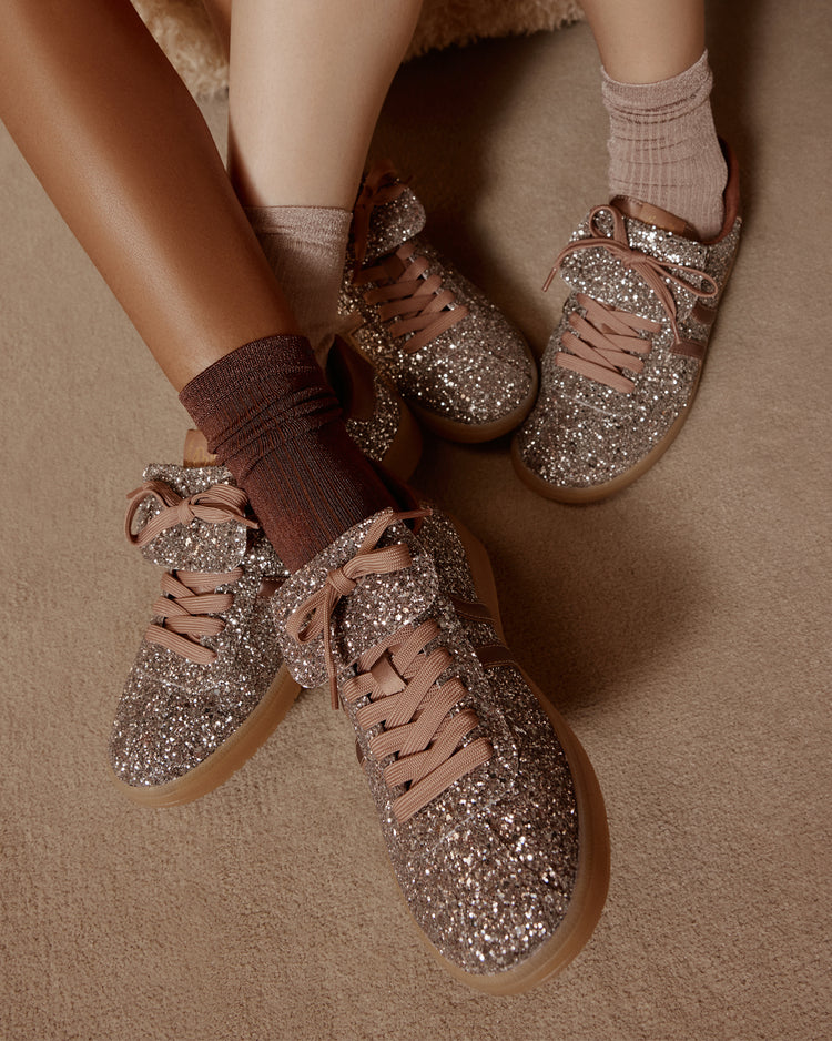 Glittery sneakers worn with brown socks on a beige surface