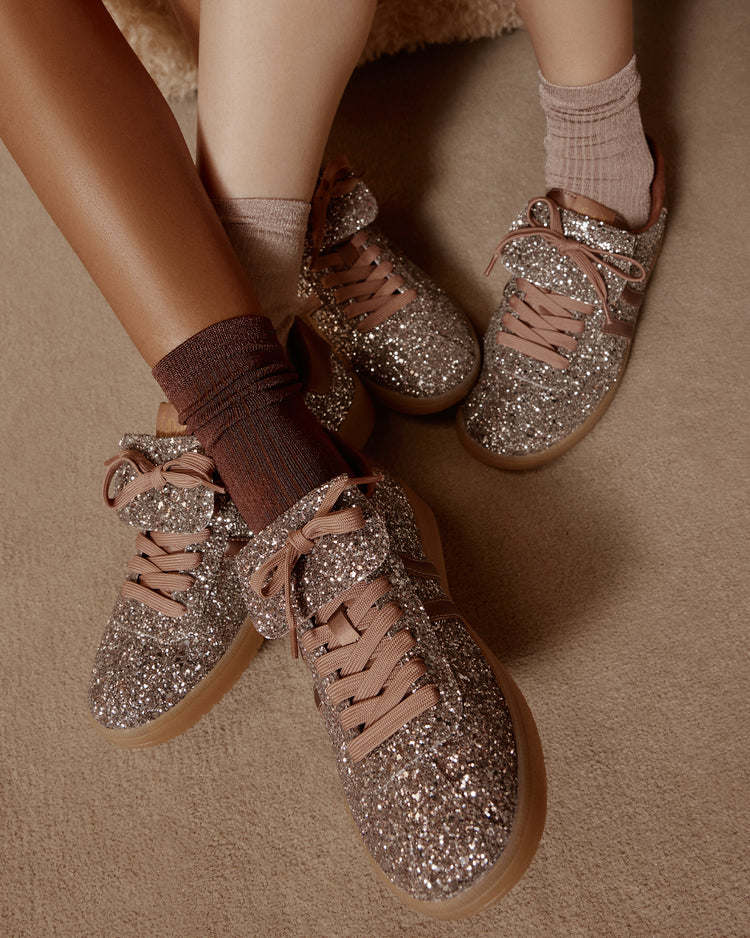 Glittery brown sneakers worn with brown socks on a beige surface