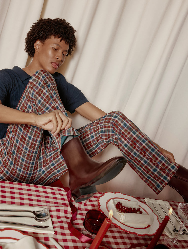 Person sitting on a couch wearing plaid pajama pants and a dark shirt, with a checkered tablecloth and candles in the foreground.
