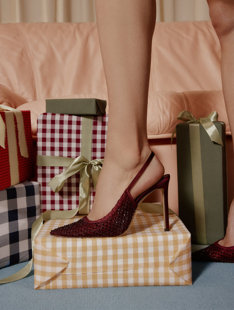 Red high-heeled shoes stepping onto a gift box with wrapped presents in the background.