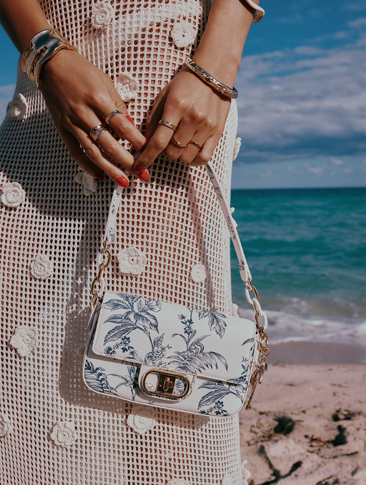 Person holding a floral handbag on a beach with ocean view.