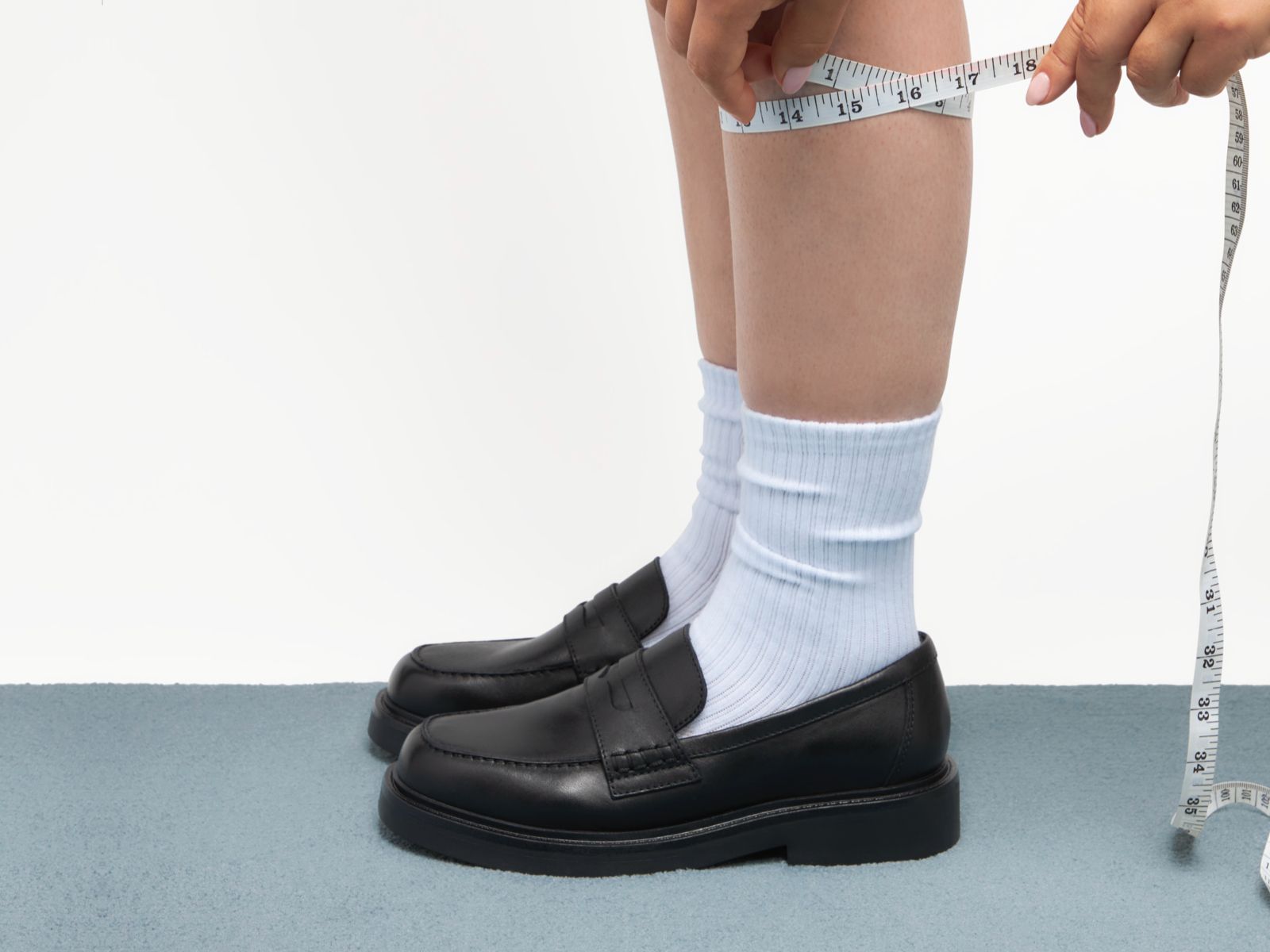 Person wearing black shoes and white socks with a measuring tape around the ankle.