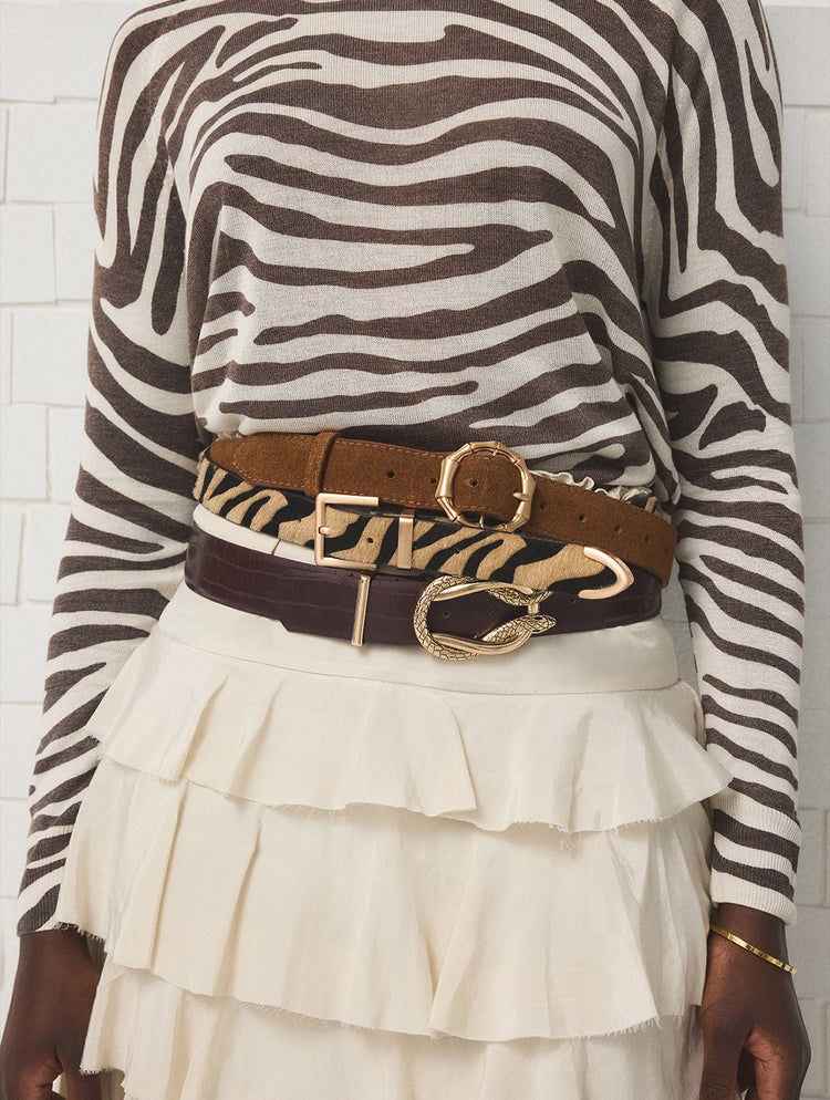 Person wearing a zebra print long-sleeve top and white ruffled skirt with a brown belt featuring a gold buckle.