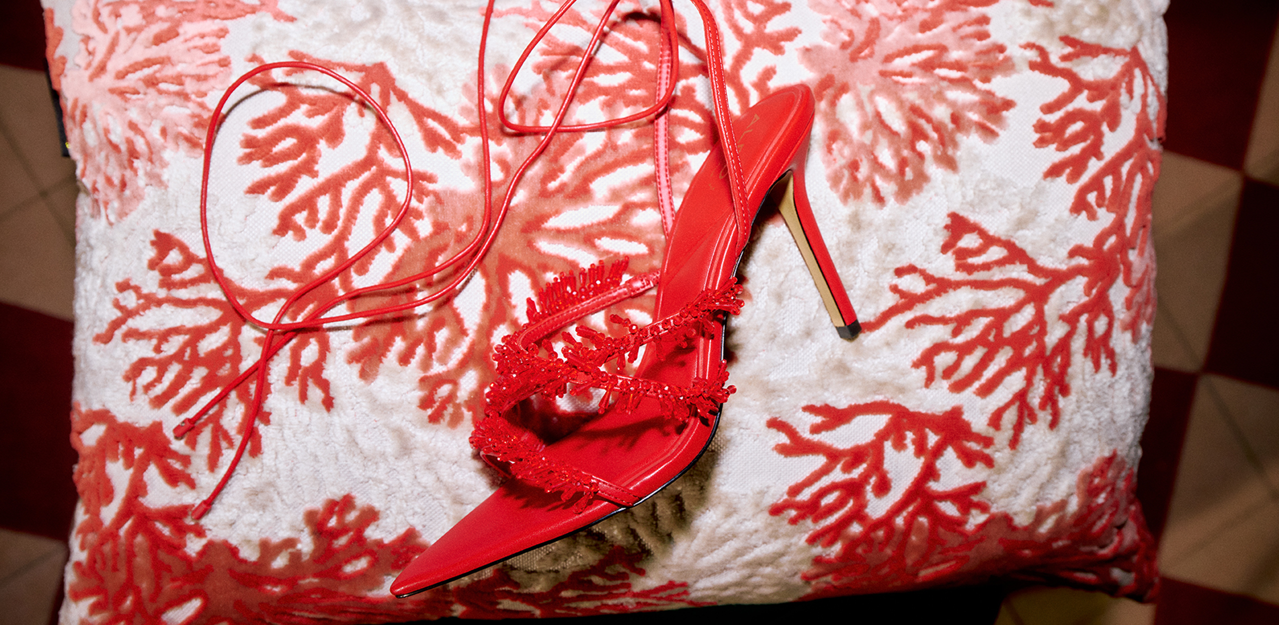Red high-heeled shoes on a pillow with red coral design.