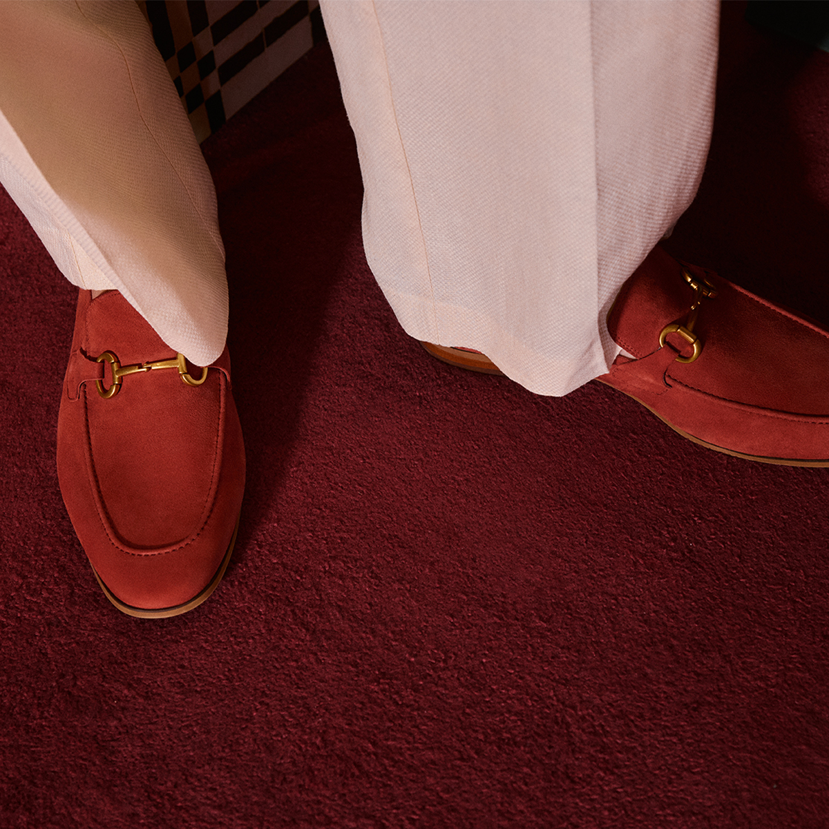 Red loafers with gold buckles worn on a red carpet