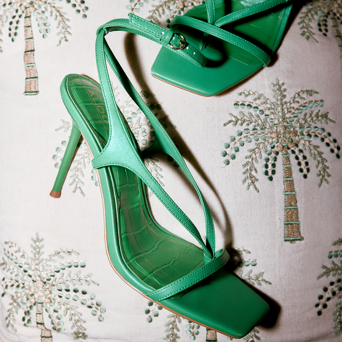 Green high-heeled sandals on a decorative fabric background.