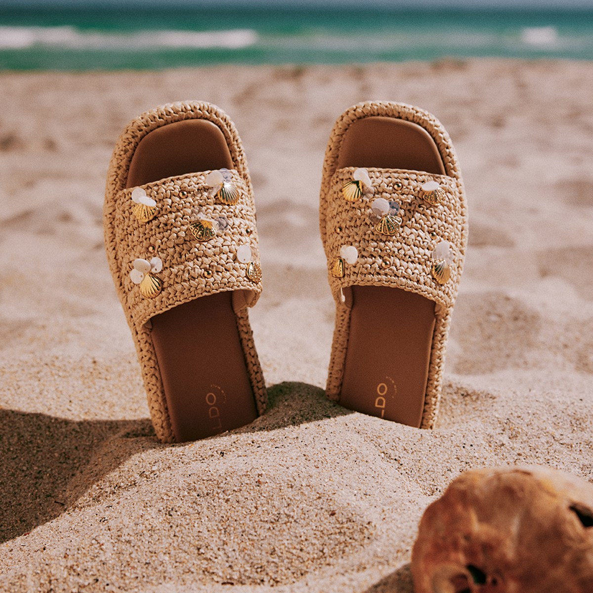 Une paire de sandales tressées ornées d’éléments décoratifs sur une plage de sable.