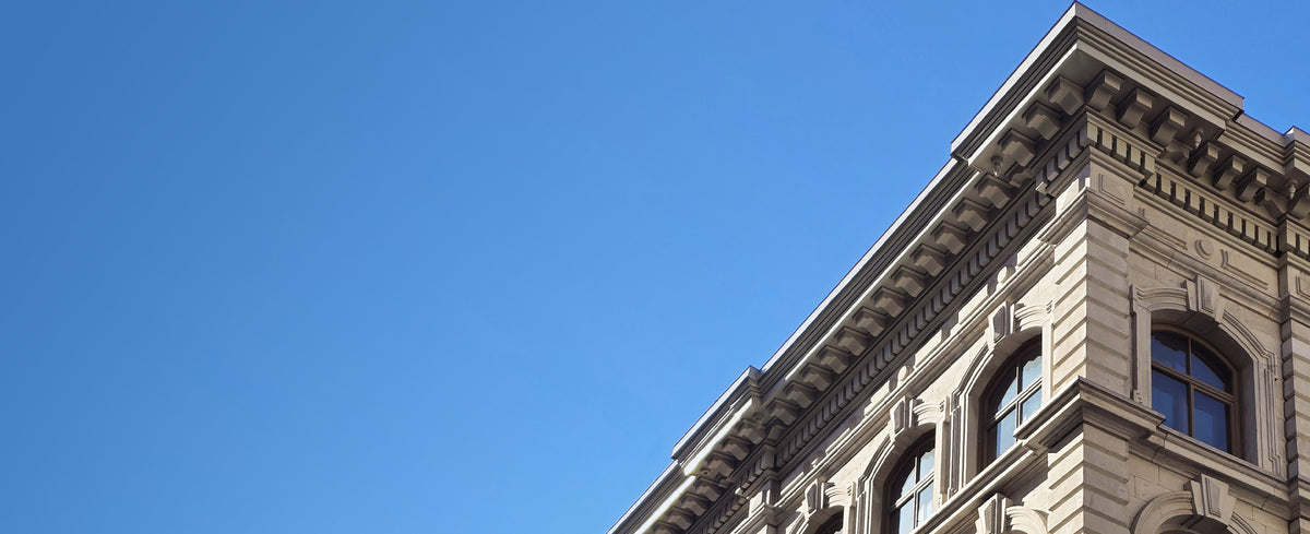 An upward view of a classical stone building corner against a clear blue sky.