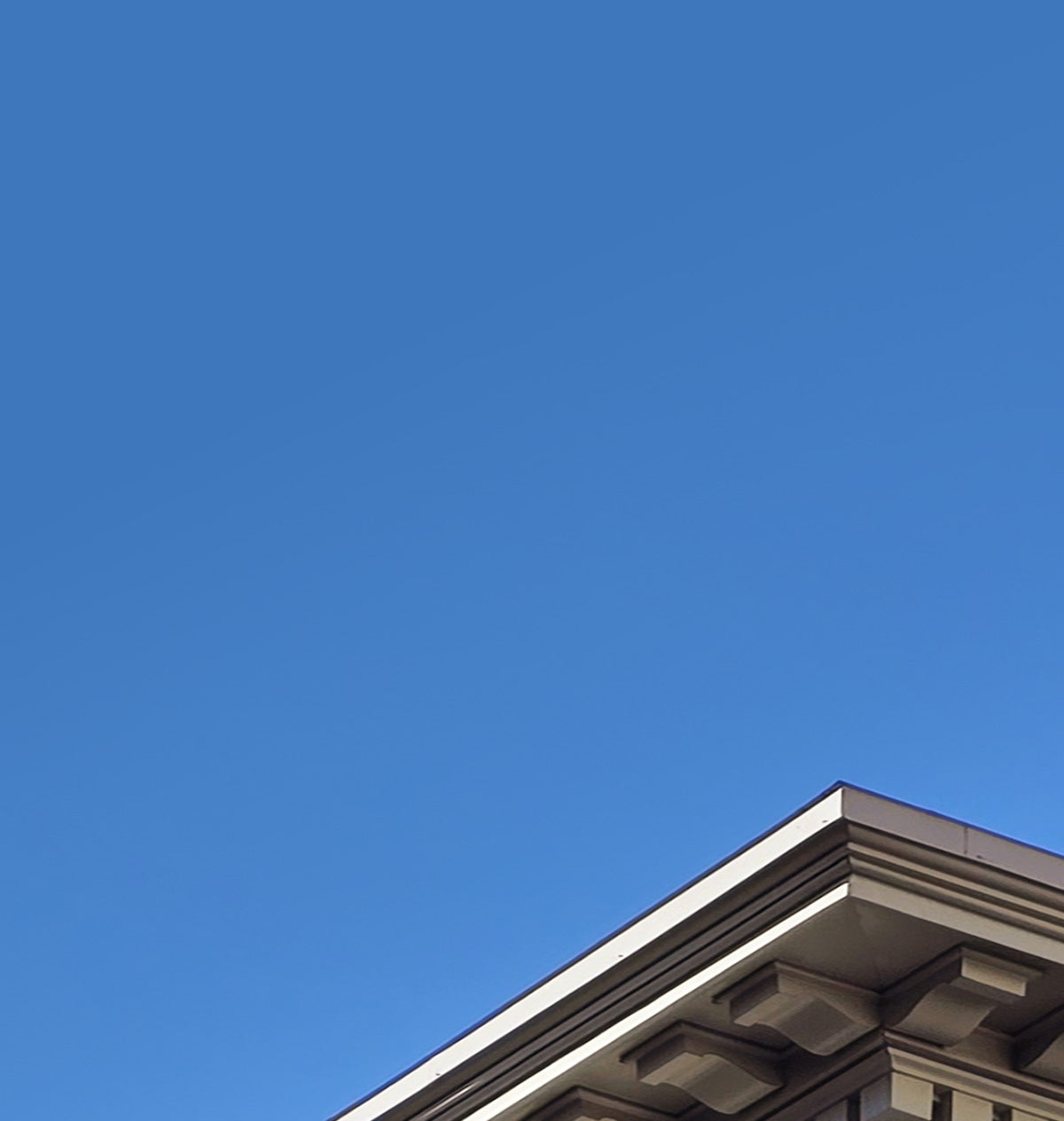 An upward view of a classical stone building corner against a clear blue sky.