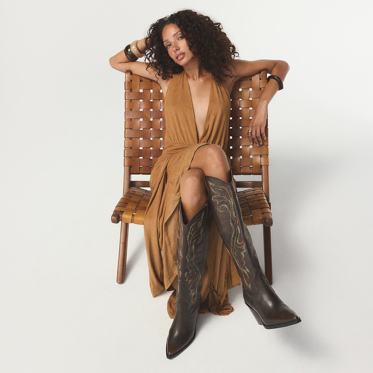 Woman wearing a brown dress and brown western boots with a white background