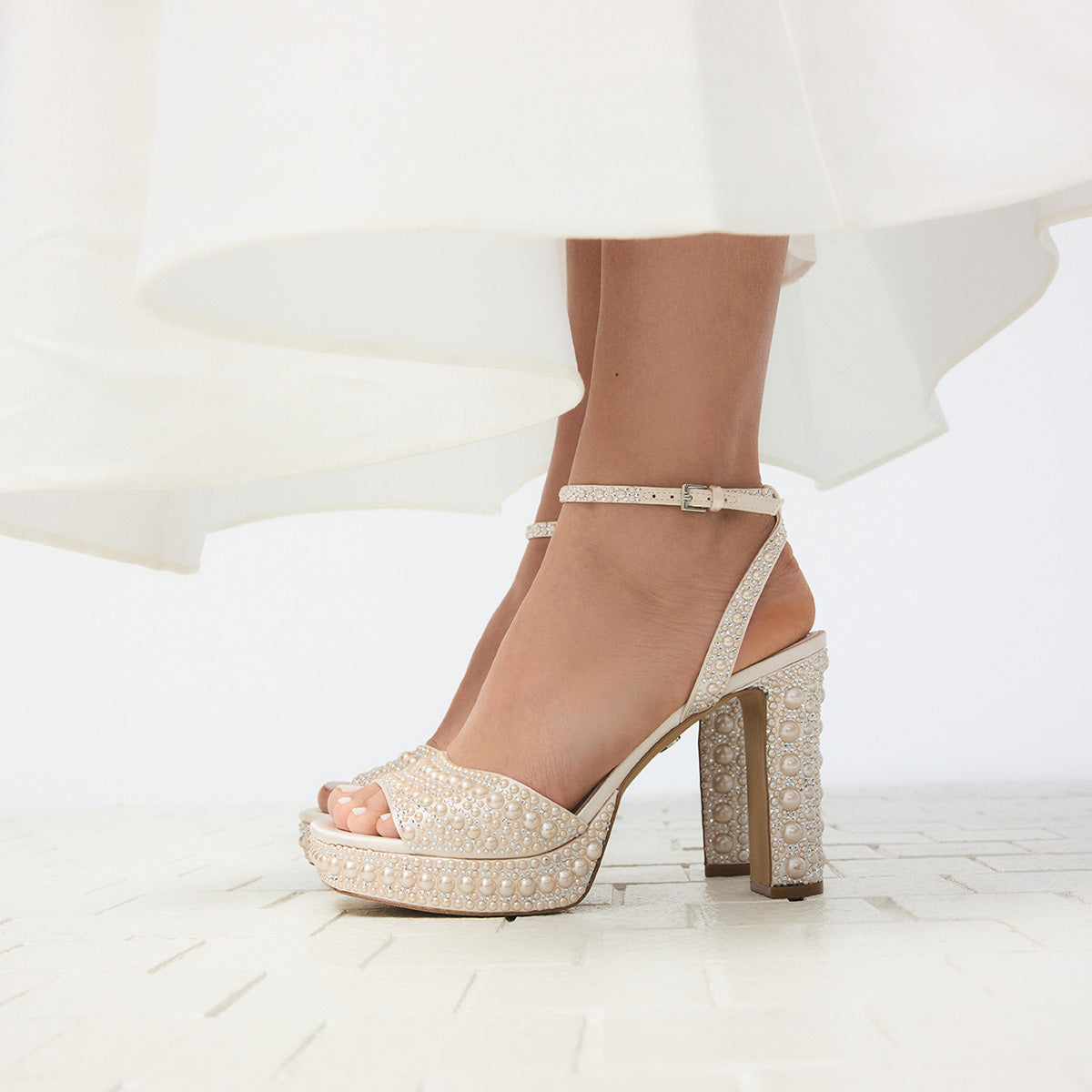 Sparkly beaded platform high heels worn with a white dress on a light background.