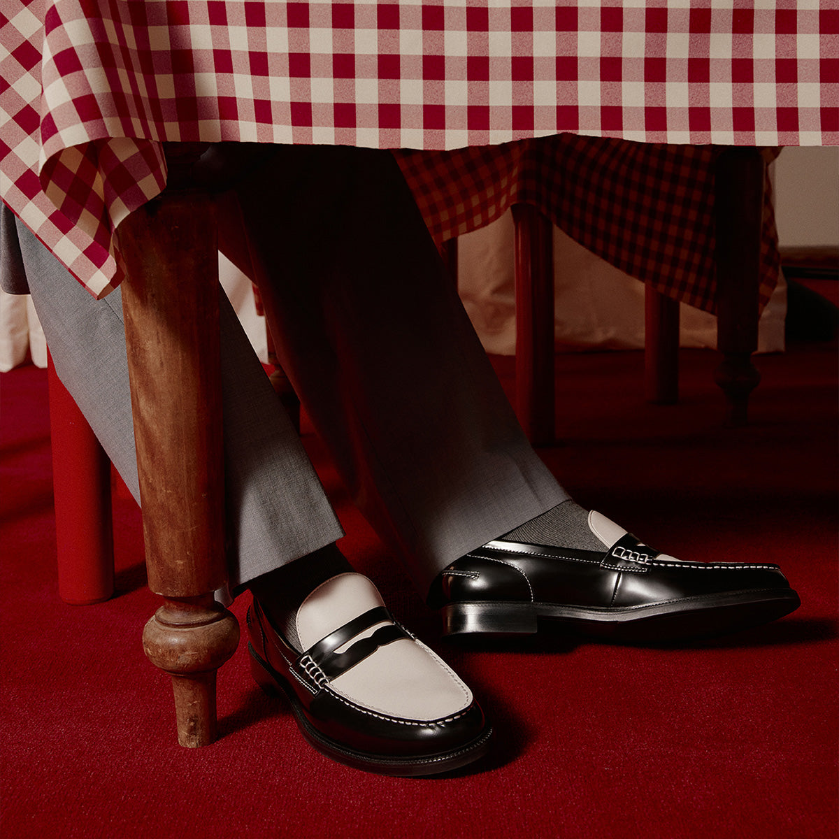 Person wearing black and white Kieran loafers sitting at a table with a red and white checkered tablecloth.