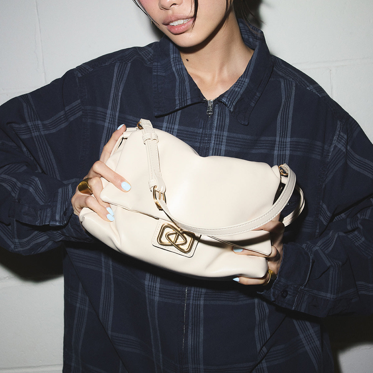 Personne tenant un sac à main blanc orné de détails dorés sur fond uni