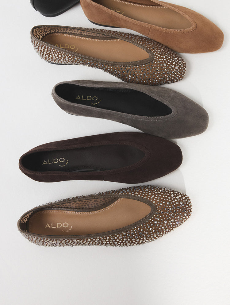 Quatre paires de ballerines ALDO en suède brun, taupe, anthracite et noir, disposées en diagonale sur un fond blanc. Les chaussures sont dotées d’un bout texturé orné de petits clous métalliques décoratifs.