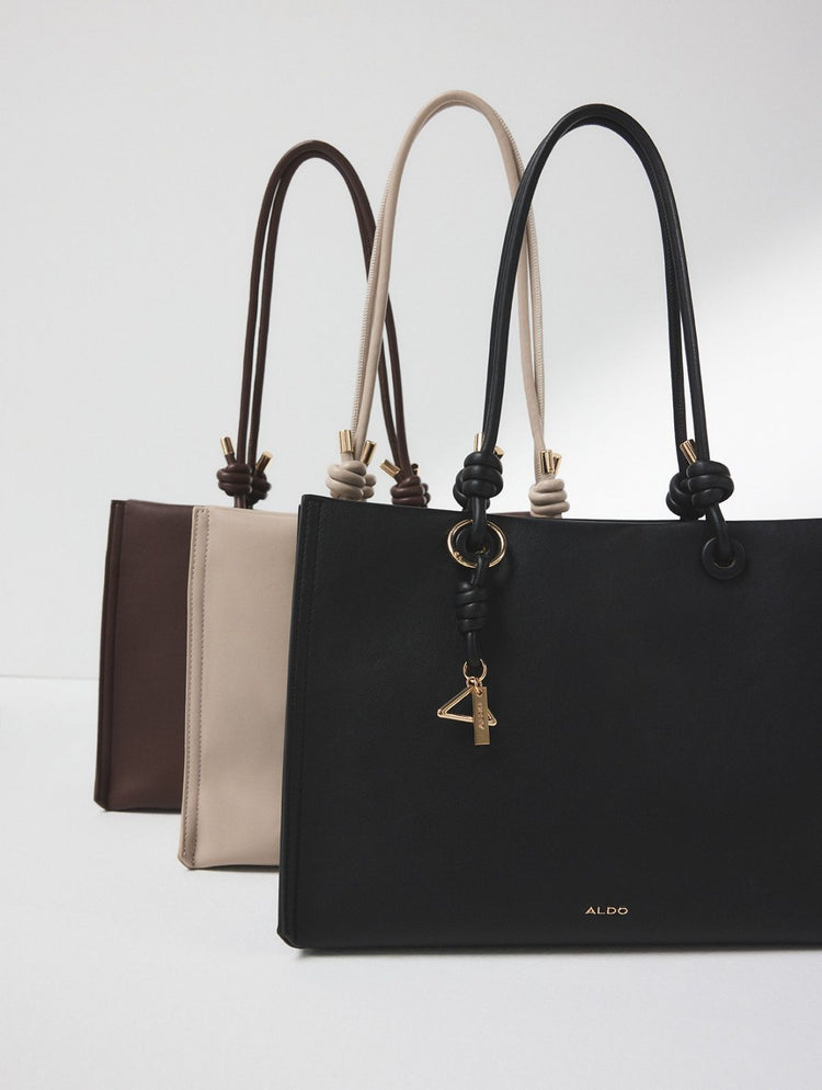 Un sac porté à l’épaule à motif serpent dans des tons de beige, brun et noir, suspendu au dossier d’une chaise noire devant un fond de studio blanc épuré.