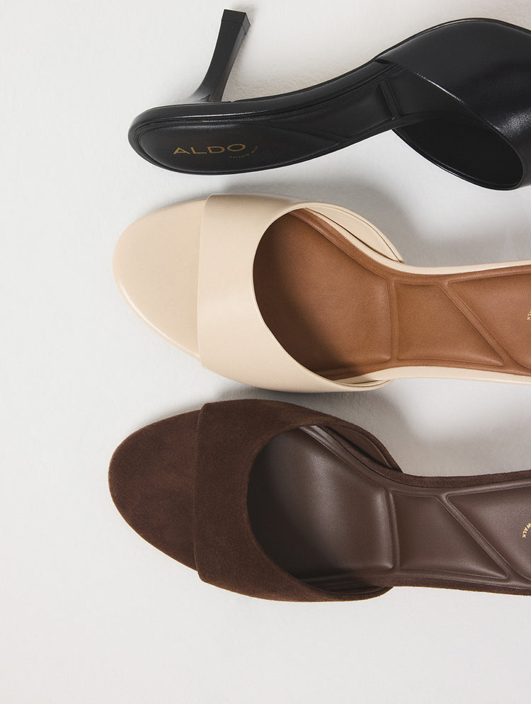 Une paire de sandales mules ALDO en noir, beige et brun, disposées en diagonale sur un fond gris pâle.