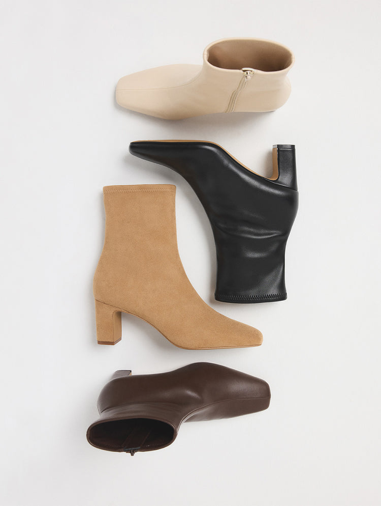 Quatre bottillons pour femme de couleurs variées (beige, noir, tan et brun), disposés en diagonale sur un fond gris pâle.