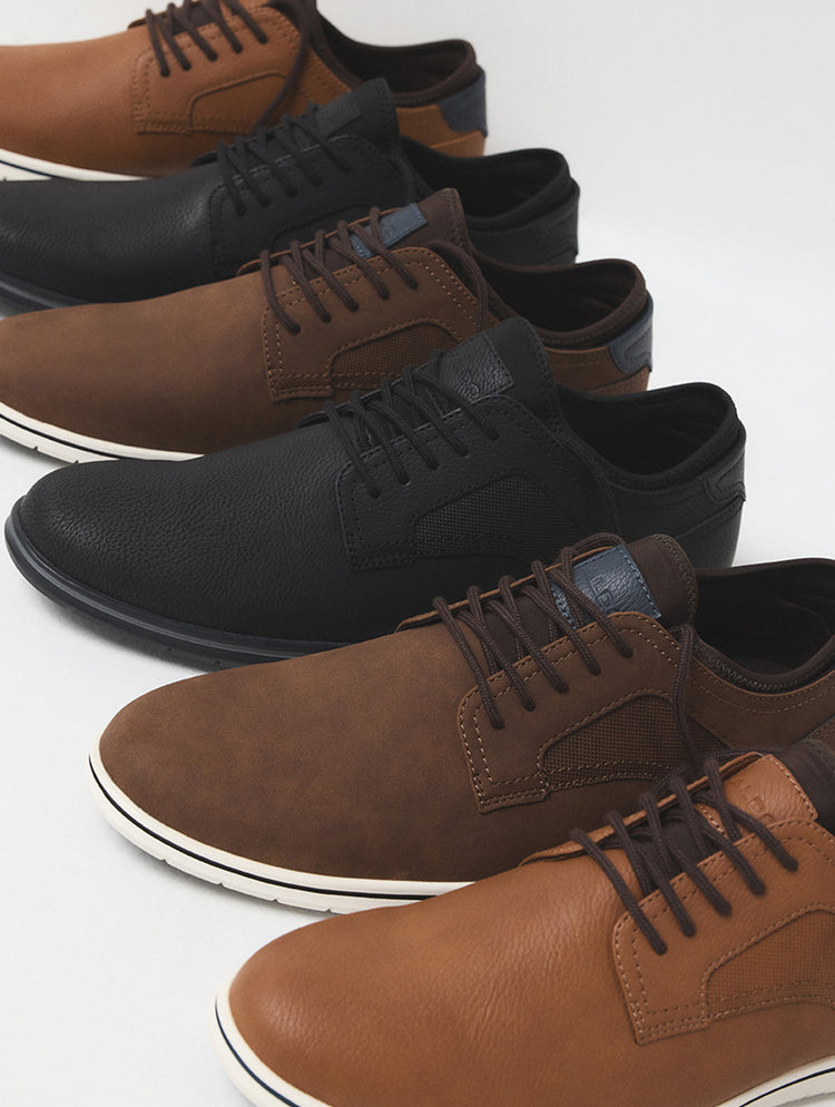 Une rangée de souliers décontractés à lacets dans des teintes de brun pâle, de brun foncé et de noir.