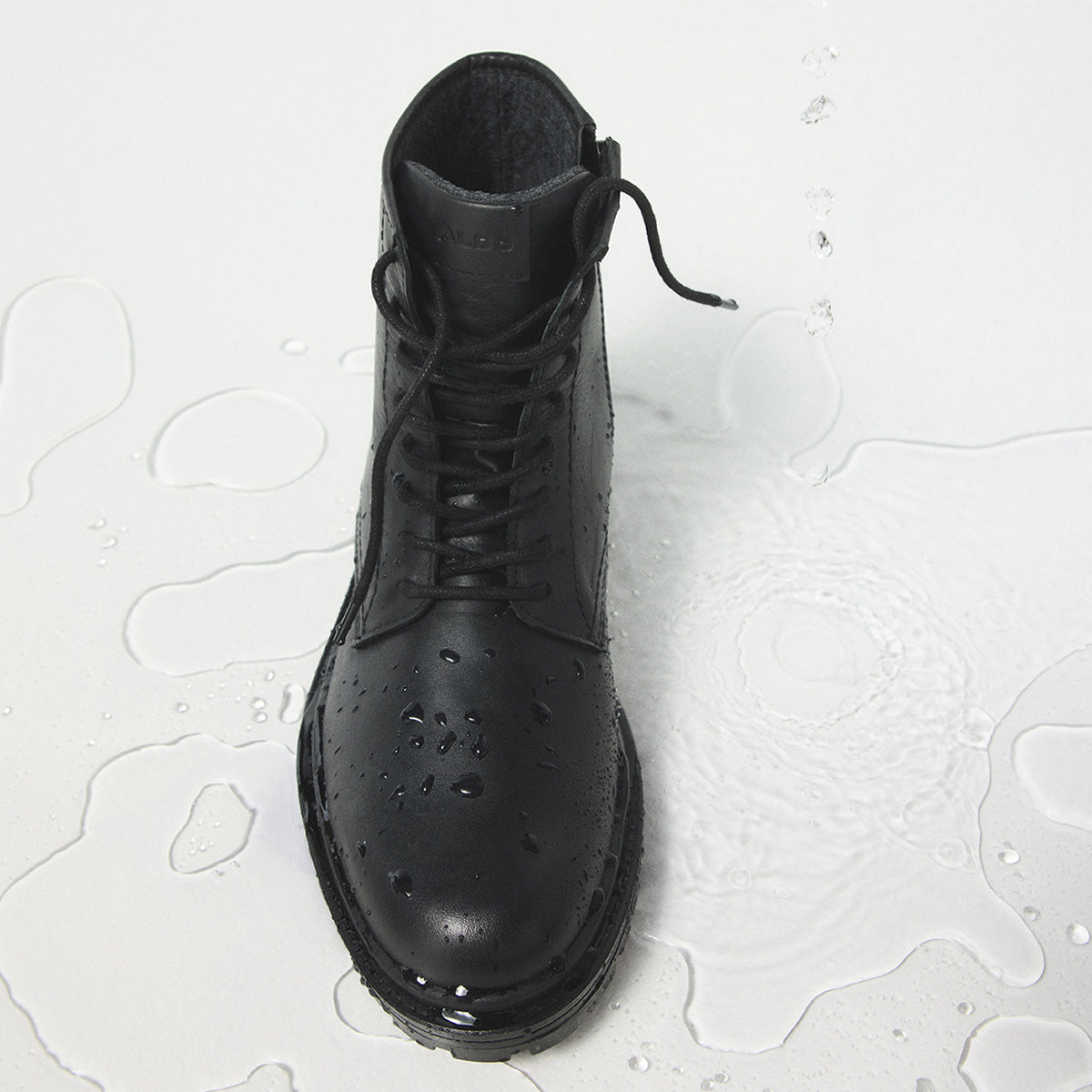 A black leather lace-up ankle boot with water droplets on the toe, set against a white background with water puddles.