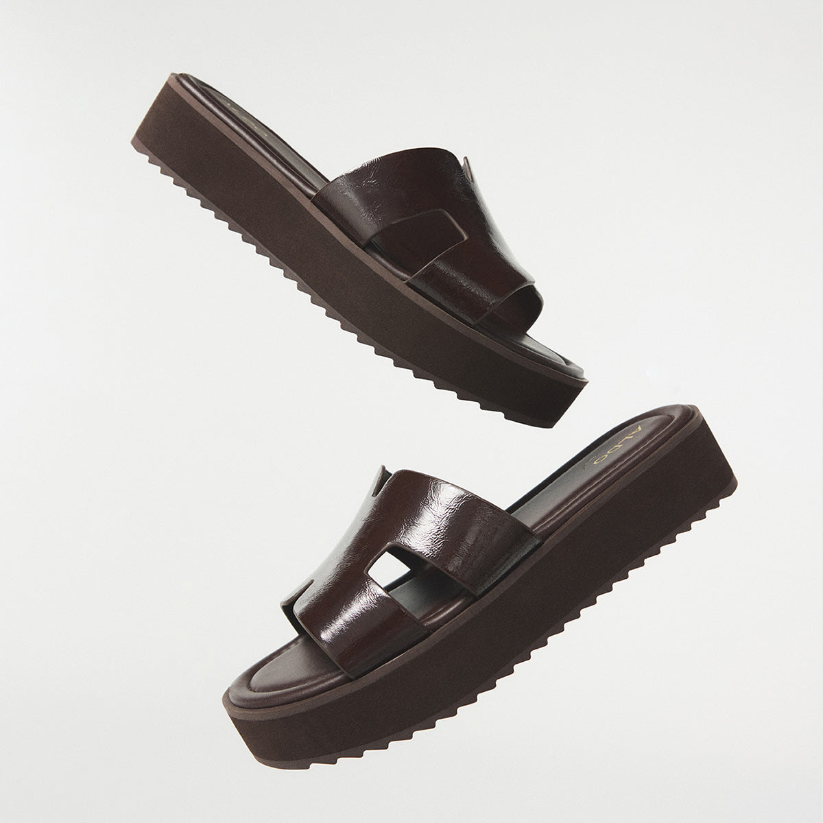 A pair of dark brown platform slide sandals with cutout straps, shown from different angles against a light gray background.