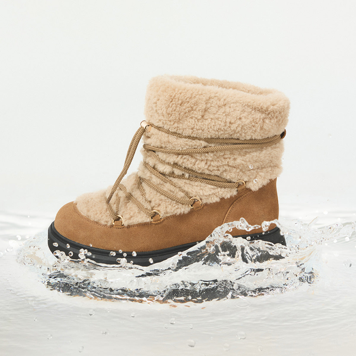 A mid-calf shearling boot in tan and beige with a thick black sole, shown stepping into splashing water against a clean white background.
