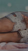 Girl laying on the beach with a crochet dress, white flat sandals and a textured handbag. 