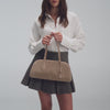 A video of a person wearing a white button-down shirt and a grey pleated skirt while carrying a beige suede shoulder bag. The video features close-up shots highlighting the bag’s zipper and design details, and concludes with the person walking out of the frame carrying the bag.