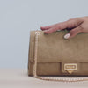 A video featuring a close-up of a hand demonstrating the functionality of a tan suede handbag with a gold-tone chain strap and gold clasp. The video highlights the adjustable chain strap and showcases the bag being securely closed. It ends with the person placing the bag on their shoulder and walking out of the frame.