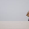 A video of a person placing a nude suede clutch on a table, followed by close-up shots showcasing its interior capacity as they place a lipstick, wallet, and sunglasses inside before closing it. The video ends with the person carrying the clutch by hand and walking out of the frame.