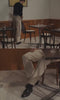 A video of a man sitting at a restaurant wearing a black sweater, taupe trousers and black loafers.