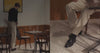 A video of a man sitting at a restaurant wearing a black sweater, taupe trousers and black loafers.