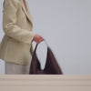 A video of a person placing a brown woven tote bag on a table, followed by close-up shots highlighting its woven texture and design details. The video then showcases the bag’s capacity as a notebook and water bottle are placed inside. It concludes with the person slipping the bag over their shoulder and walking out of the frame.