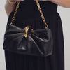 A video of a person holding and opening a black handbag that has a gold round clasp.