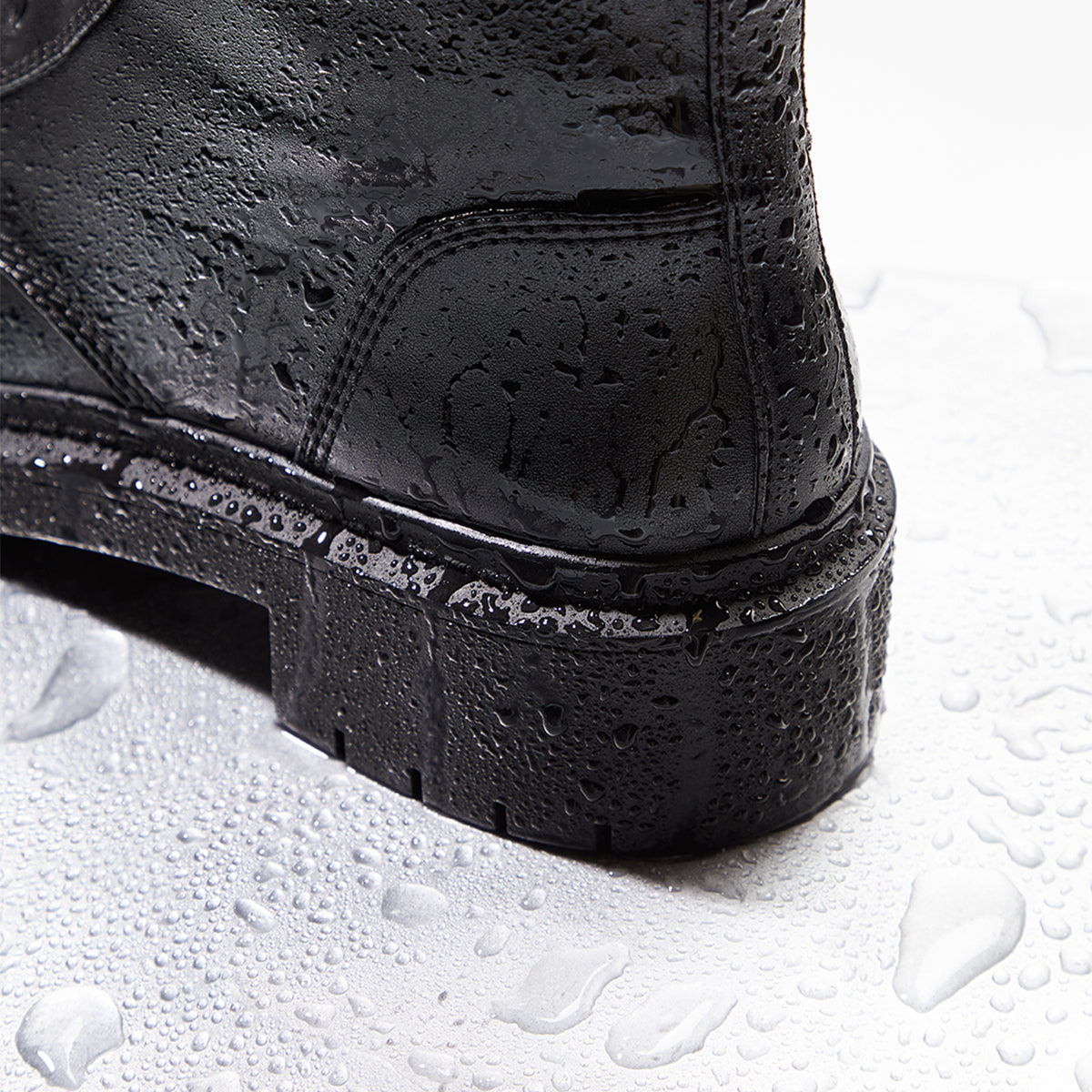 Close-up of a black boot sole on a white background with water droplets.